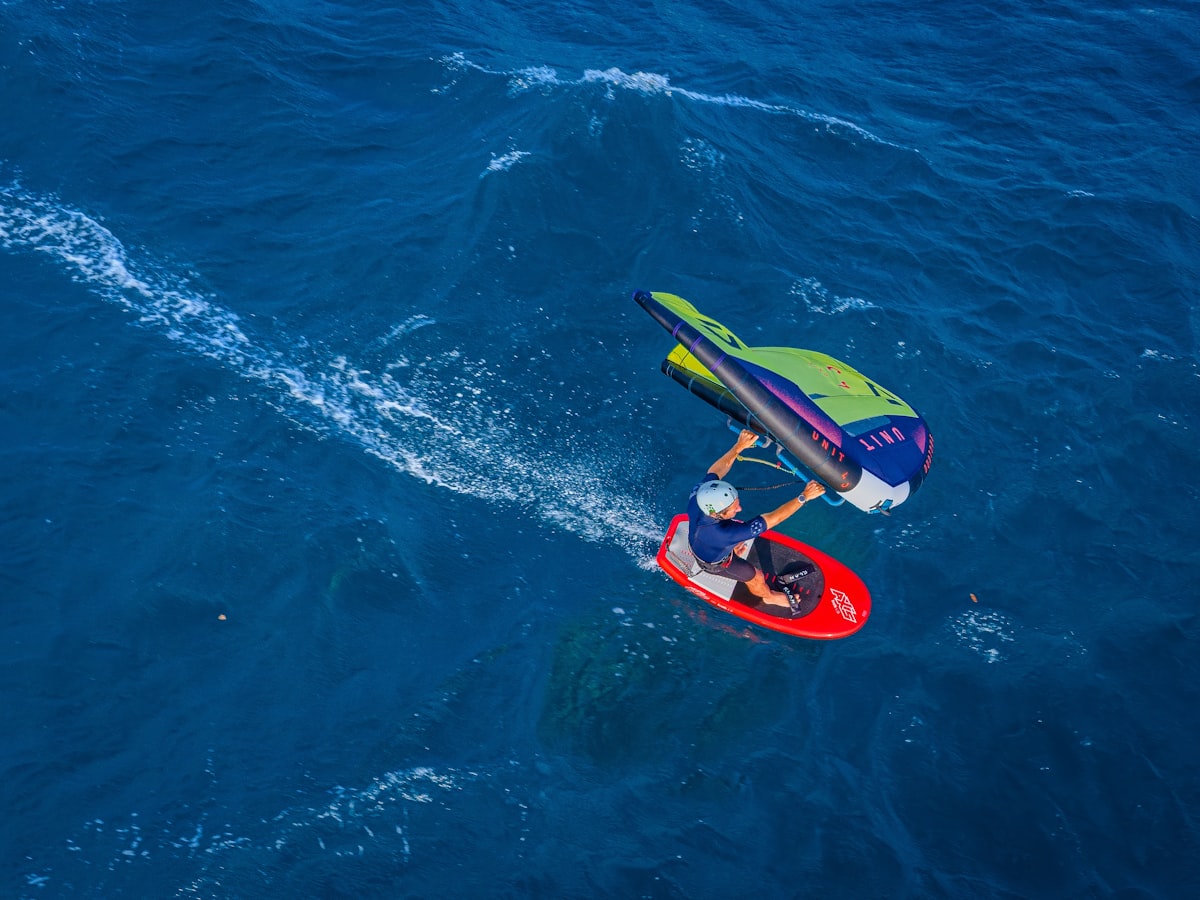 Wing foiler carving across deep blue ocean, seen from above